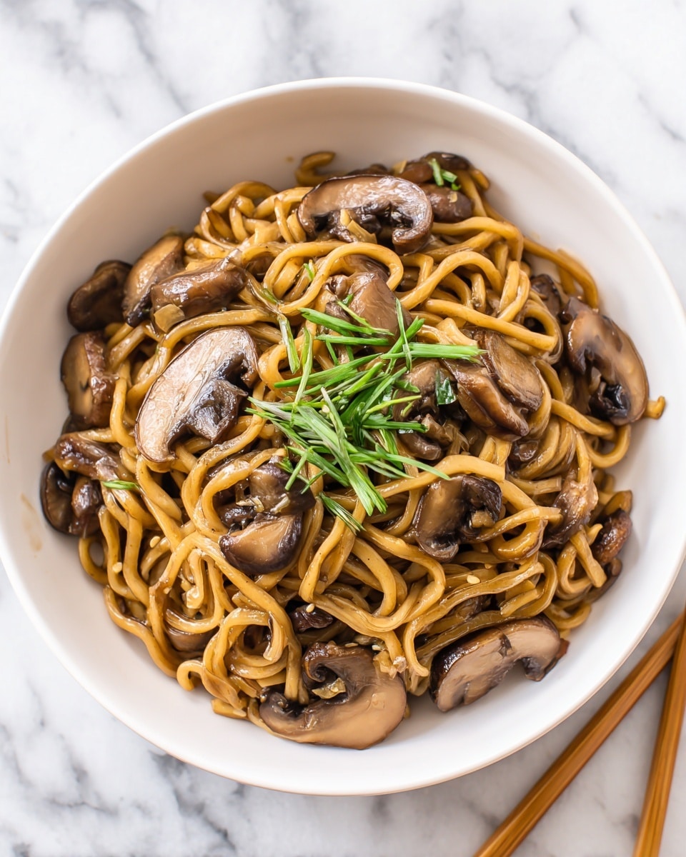 A bowl filled with creamy brown noodles mixed with sliced mushrooms, showing thick and slightly glossy textures. The noodles are swirling around with mushroom pieces of varying sizes, some whole and some sliced, with a light brown color and smooth texture. On top sits a small bunch of thin green sliced herbs for garnish. The bowl is white and rests on a white marbled surface with a pair of wooden chopsticks partially visible on the side. photo taken with an iphone --ar 4:5 --v 7