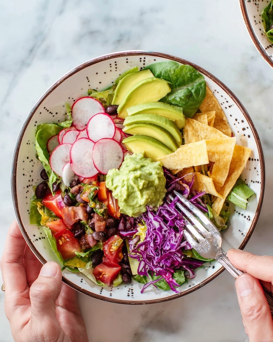 A white bowl with black dots is filled with a colorful salad that has multiple layers: at the bottom are fresh green leafy lettuce, topped with sliced cherry tomatoes and thin round radish slices. Above this are strips of crispy tortilla, black beans scattered, and bright purple shredded cabbage. On top, there are several slices of creamy light green avocado arranged in a fan shape, a spoonful of thick green sauce, and small chunks of red tomatoes. A woman's hand holds the bowl on the left side, and another woman's hand with a fork is about to scoop the salad from the right side. The bowl sits on a white marbled surface with a blue and white striped cloth nearby, with a glass of green liquid and a small jar of green sauce in the background. photo taken with an iphone --ar 4:5 --v 7