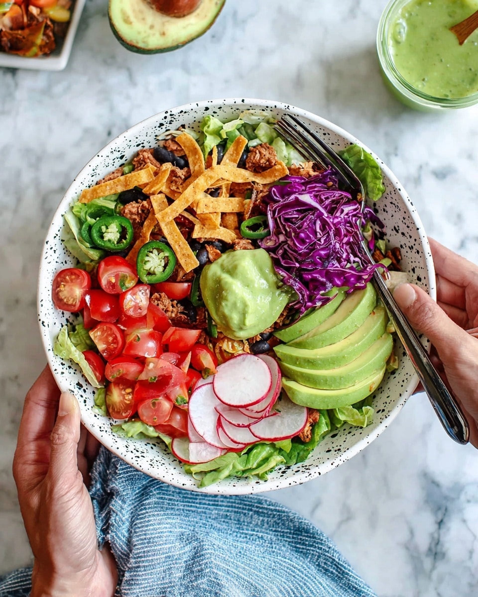 The image shows a white bowl with black dots filled with a colorful layered salad. The bottom layer is fresh green lettuce. On top are sliced bright red cherry tomatoes, thin round radish slices, and green jalapeño slices. There are strips of crunchy tortilla, black beans, and bits of cooked seasoned meat scattered throughout. A mound of shredded purple cabbage sits to one side, along with a small pile of diced red tomatoes. Five slices of creamy green avocado fan out near the center, next to a dollop of thick green sauce. Two woman's hands hold the bowl, one on the side and the other holding a fork with some salad. The bowl sits on a white marbled surface with a blue and white striped cloth nearby. Photo taken with an iphone --ar 4:5 --v 7