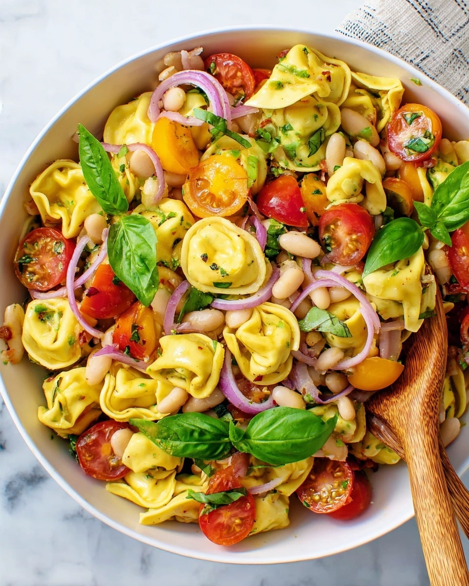 The dish is a bright pasta salad served in a white bowl on a white marbled surface. The base layer is small yellow tortellini pasta, soft and plump, spread all around. Mixed with the pasta are halved red and yellow cherry tomatoes, adding vibrant spots of color. Thin slices of purple onion are scattered on top, giving a slight curve and contrast. There are fresh green basil leaves placed evenly around, adding texture and freshness. White beans are also mixed in, small and smooth, filling the spaces between pasta and veggies. Wooden spoons rest inside the bowl, blending naturally with the salad. photo taken with an iphone --ar 4:5 --v 7