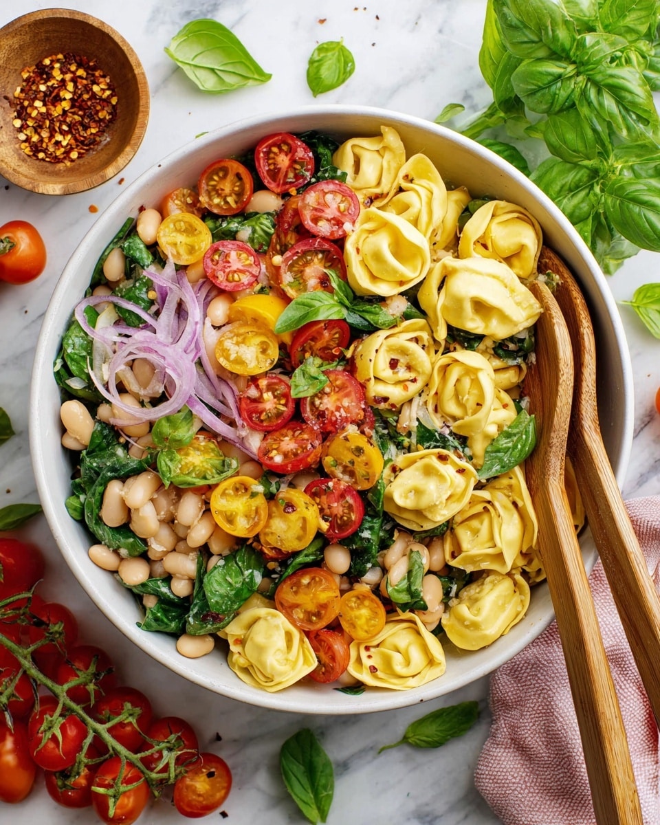 The image shows a white bowl filled with a colorful pasta salad. The bottom layer is pale yellow tortellini pasta pieces with soft textures. Mixed in are sliced red and yellow cherry tomatoes, some cut in half showing juicy insides. Thin slices of purple-red onion are scattered around, adding color and slight sharpness. White beans are spread evenly in the bowl, giving a soft, round texture. Fresh green basil leaves are placed on top, adding a bright green color and a fresh look. Two wooden spoons rest inside the bowl, partially covered by the salad. The overall background is a white marbled surface. Photo taken with an iphone --ar 4:5 --v 7