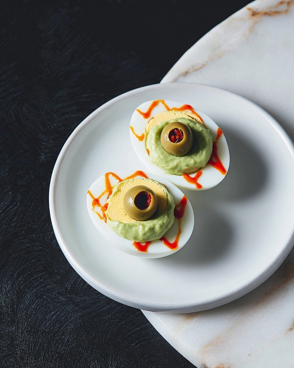 Two halves of a hard-boiled white egg are placed on a white plate on a white marbled surface. Each egg half is topped with a thick, light green layer of smooth avocado mash. A green olive with a small piece of red pimento in the center sits on top of the avocado layer. Thin, squiggly lines of orange sauce are drawn on the egg white, radiating outward from the avocado layer. The photo taken with an iphone --ar 4:5 --v 7