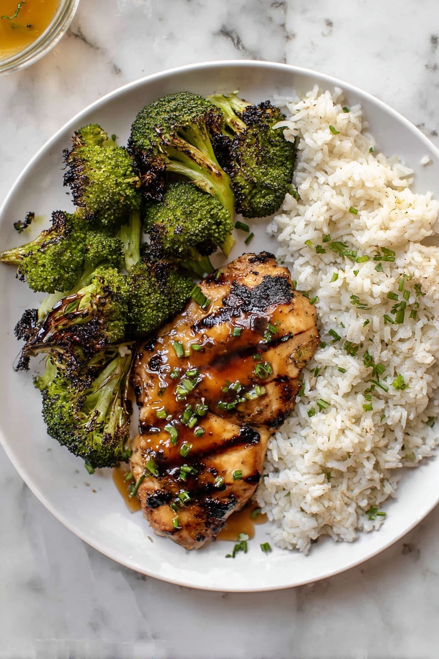 Grilled Honey Mustard Chicken and Broccoli, honey mustard chicken, healthy grilled chicken recipes, easy weeknight dinner ideas, flavorful grilled broccoli - A white plate holds four grilled chicken pieces arranged in the top half, each with dark, distinct grill marks and a shiny glaze, sprinkled with small green chopped herbs. Below the chicken, roasted broccoli florets with dark charred spots cover the bottom half of the plate, showing a mix of bright and deep green colors. The plate is set on a white marbled surface, and a small white bowl with plain cooked rice is partially visible in the bottom left corner. Photo taken with an iphone --ar 2:3 --v 7