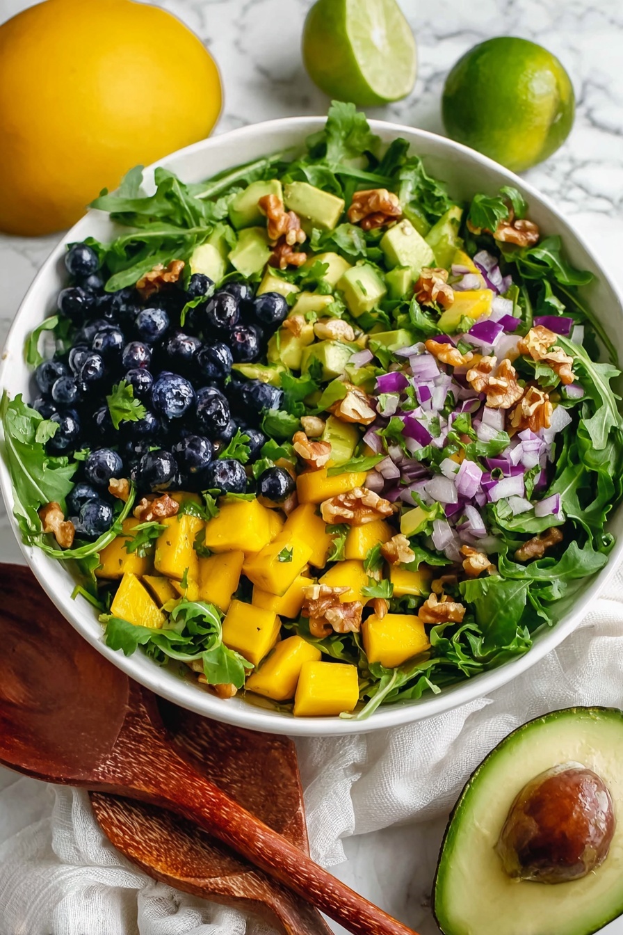 Mango Cucumber Salad with Blueberries and Avocado, fresh tropical fruit salad, easy healthy summer salad, vegan fruit salad recipes, quick fruit salad ideas - A round white plate is filled with a fresh salad that has several layers. The base layer is made of bright green arugula leaves with long thin shapes. On top, there are small cubes of yellow mango and chunks of light green avocado scattered evenly. Dark blue blueberries and chopped purple onion pieces add color contrast, along with light brown walnut pieces that add texture. Small cilantro leaves are sprinkled across the salad. The plate is placed on a white marbled surface with whole limes, mangoes, blueberries, and half an avocado around it. photo taken with an iphone --ar 2:3 --v 7