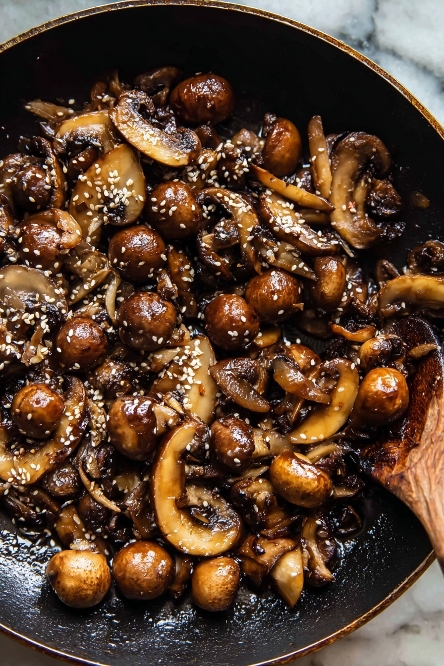 Saucy Ginger Sesame Noodles with Caramelized Mushrooms, quick Asian noodle recipes, easy weeknight dinner ideas, flavorful mushroom noodle stir-fry, 30-minute Asian noodles - The image shows a black pan filled with cooked mushrooms, including both sliced brown mushrooms and whole small mushrooms with a glossy, browned surface. There are small white sesame seeds sprinkled on top, adding texture, and the mushrooms appear lightly caramelized with a slightly crispy look. On the right side of the pan, a wooden spoon is partially visible, resting among the mushrooms. The background surface is a white marbled texture. photo taken with an iphone --ar 2:3 --v 7