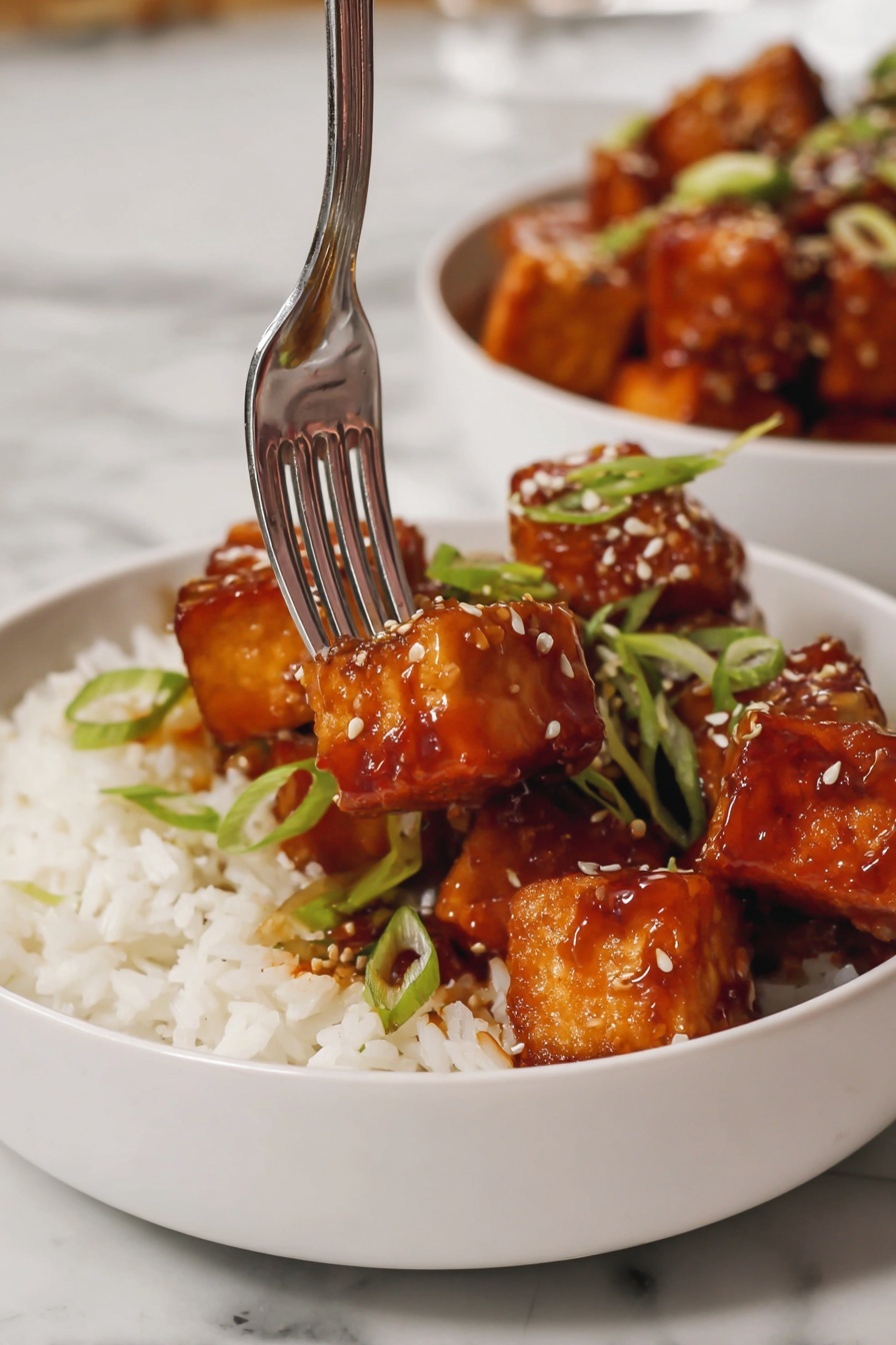 Crispy Air Fryer Tofu with Spicy Chili Mayonnaise, crispy tofu recipes,air fryer tofu ideas, spicy tofu sauce, healthy vegan tofu dishes - A white bowl filled with fluffy white rice forms the base layer, topped with several medium-sized golden brown tofu cubes coated in a shiny, thick reddish-brown sauce. The tofu pieces are garnished with thin, bright green sliced scallions and scattered light-colored sesame seeds. A shiny silver fork is picking up one tofu cube from the bowl, and there is a second white bowl with more sauced tofu cubes in the blurry background, all set on a white marbled surface. photo taken with an iphone --ar 2:3 --v 7