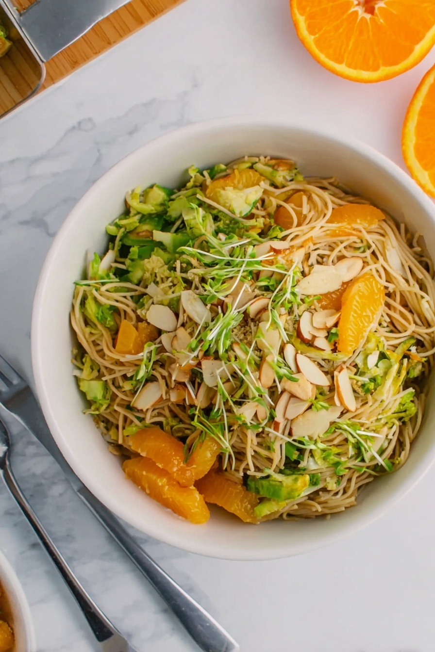 Orange Sesame Chicken Salad, healthy chicken salad with oranges, citrus chicken salad, quick chicken salad recipe, flavorful fruit and chicken salad - A white bowl filled with a noodle salad that has three visible layers: the bottom layer is light brown noodles, the middle layer has bright green sliced vegetables and small chunks of light brown tofu, and the top layer is sprinkled with thin almond slices and green herbs. On the top left side of the image, there is a half orange slice and a small piece of fresh ginger on a white marbled surface. A silver fork rests on the right side of the bowl, and a small red object is slightly visible at the far right. The photo taken with an iphone --ar 2:3 --v 7