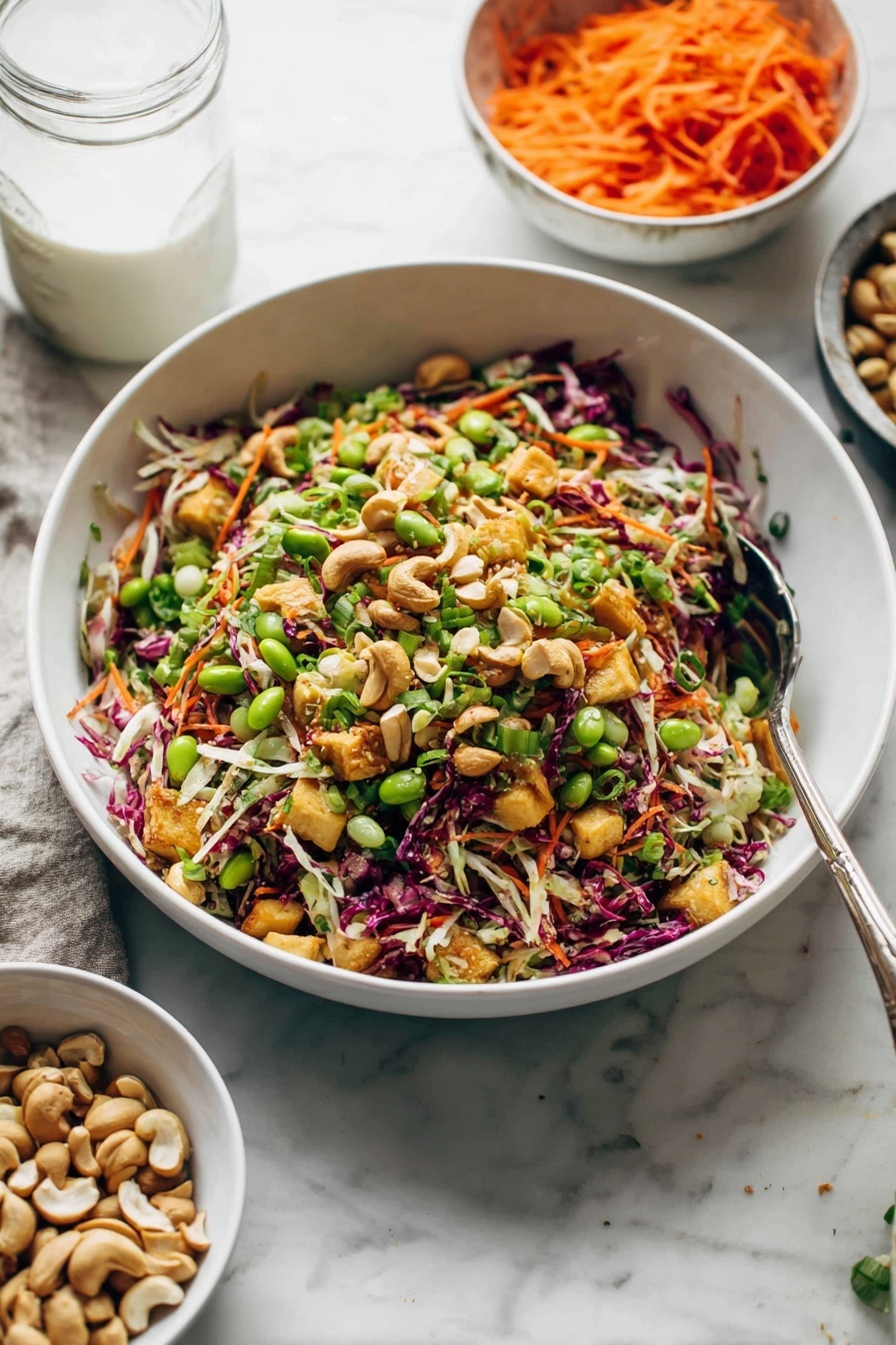 Cashew Crunch Salad with Sesame Dressing, healthy crunchy salads, easy vegetable salads, flavorful sesame salad dressing, vegetarian salad recipes - A large white bowl filled with colorful salad sits on a white marbled surface. The salad has several layers: shredded green and purple cabbage mix, bright orange shredded carrots, light green edamame beans, pieces of cooked golden brown chicken, and chopped green herbs sprinkled throughout. Whole cashew nuts are scattered on top, adding texture and a light beige color. Two silver serving spoons rest inside the bowl, ready for serving. In the background, a smaller white bowl holds more cashews, while a few cashews lay beside the main bowl. photo taken with an iphone --ar 2:3 --v 7