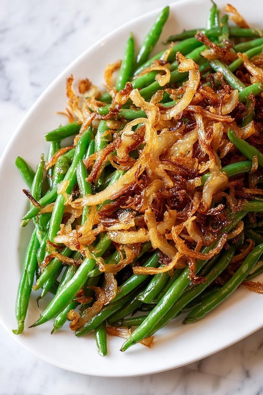 Roasted Green Beans with Caramelized Onions, green bean side dish, caramelized onion green beans, healthy roasted green beans, easy green bean recipes - The image shows a close-up of a dish made with green beans and caramelized onions. The bottom layer is bright green beans, cooked but still fresh-looking, with smooth textures and a slight shine. On top, there is a thick layer of curly, thinly sliced caramelized onions in shades of golden brown and deep amber, giving a crispy and slightly charred texture. The onions are scattered unevenly, showing both whole rings and smaller pieces. The whole dish rests on a white marbled surface that adds a clean and elegant look. Photo taken with an iphone --ar 2:3 --v 7